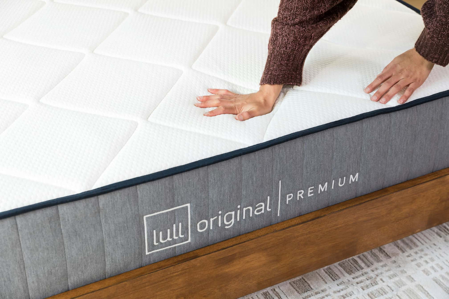 2 hands pushing down on a lull mattress showcasing its medium firmness and motion distribution.