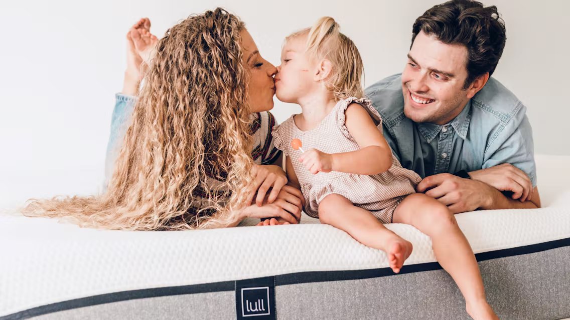 A baby girl kissing her mom on top of a lull mattress.