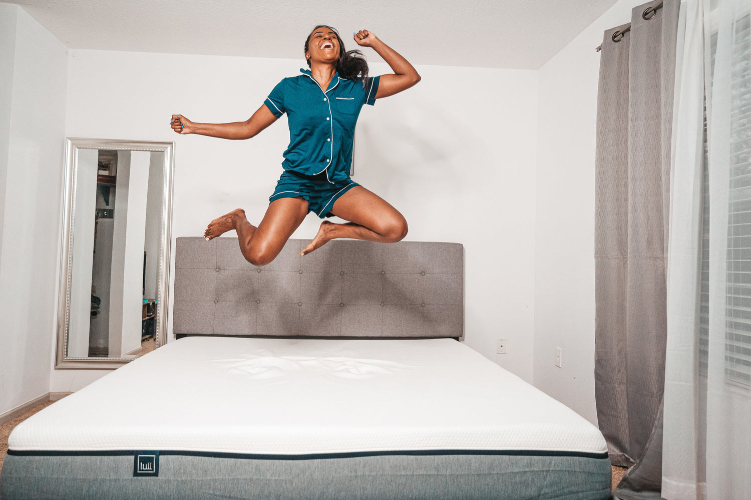 A girl smiling on her lull mattress and jumping high in the air.