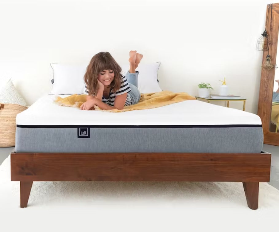 A woman laying on top of a lull mattress smiling looking down at her mattress.