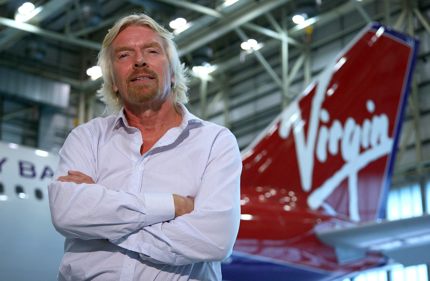Richard Branson posing in front of a Virgin airplane.