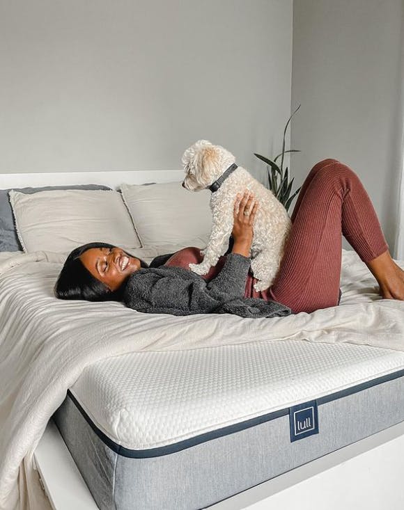 A woman lying on a Lull mattress with her dog on her lap.