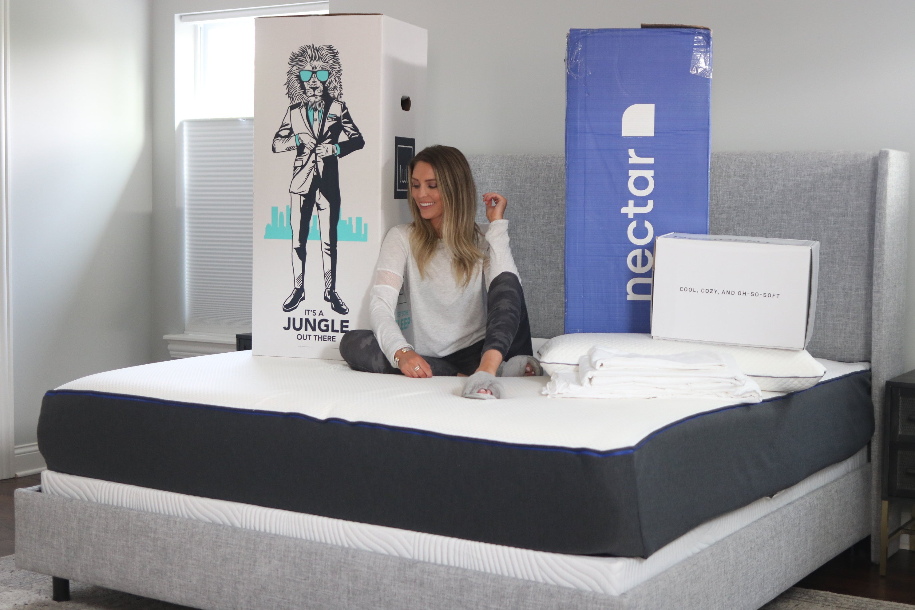 Load video: A woman sitting on a mattress smiling with a lull box and nectar box behind her.