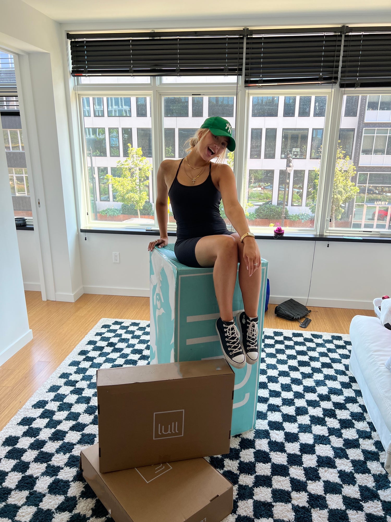 A girl sitting on top of a Lull box smiling in a sunny apartment.