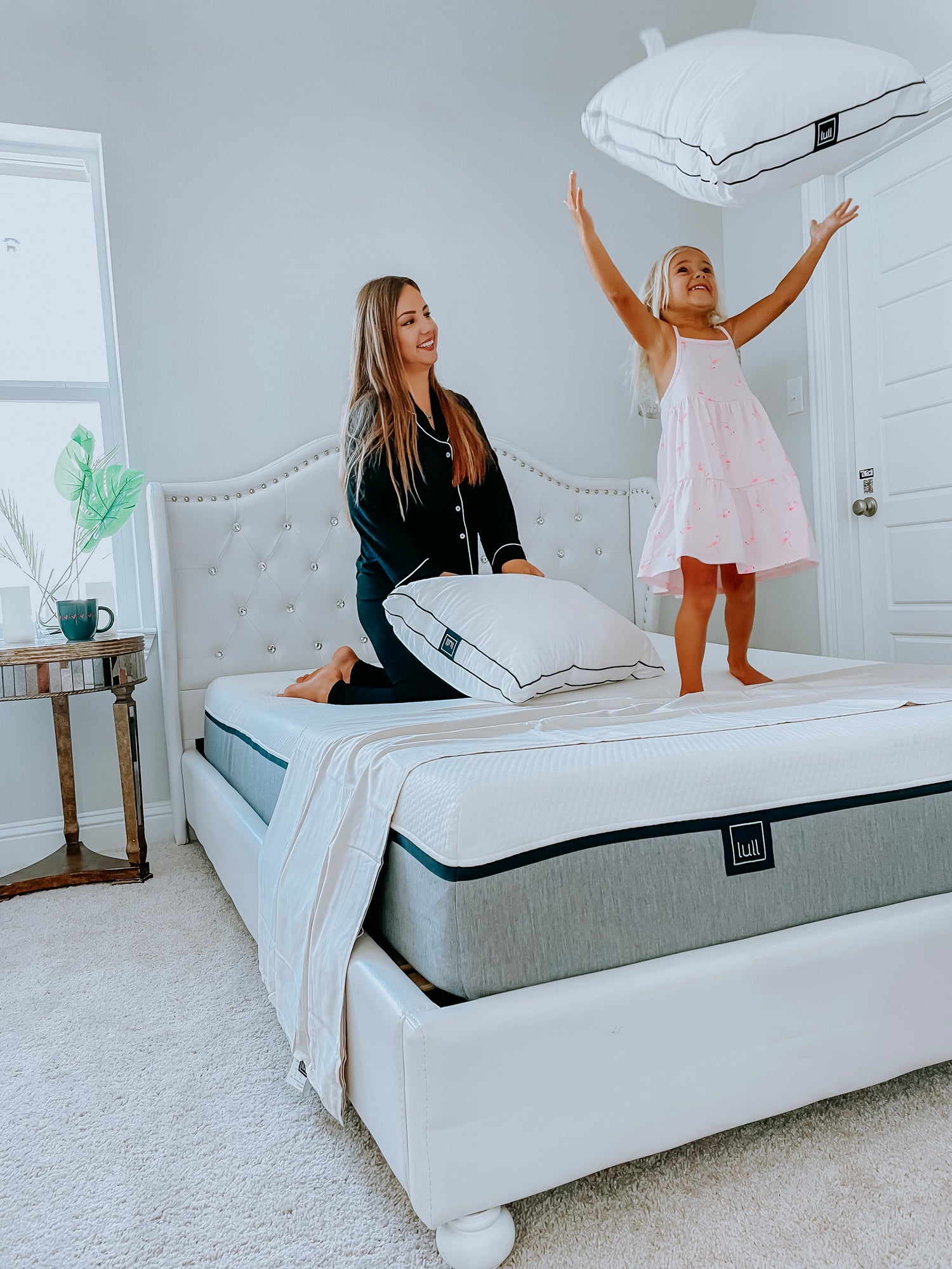 A mother and daughter on a lull mattress smiling and throwing a lull pillow in the air.