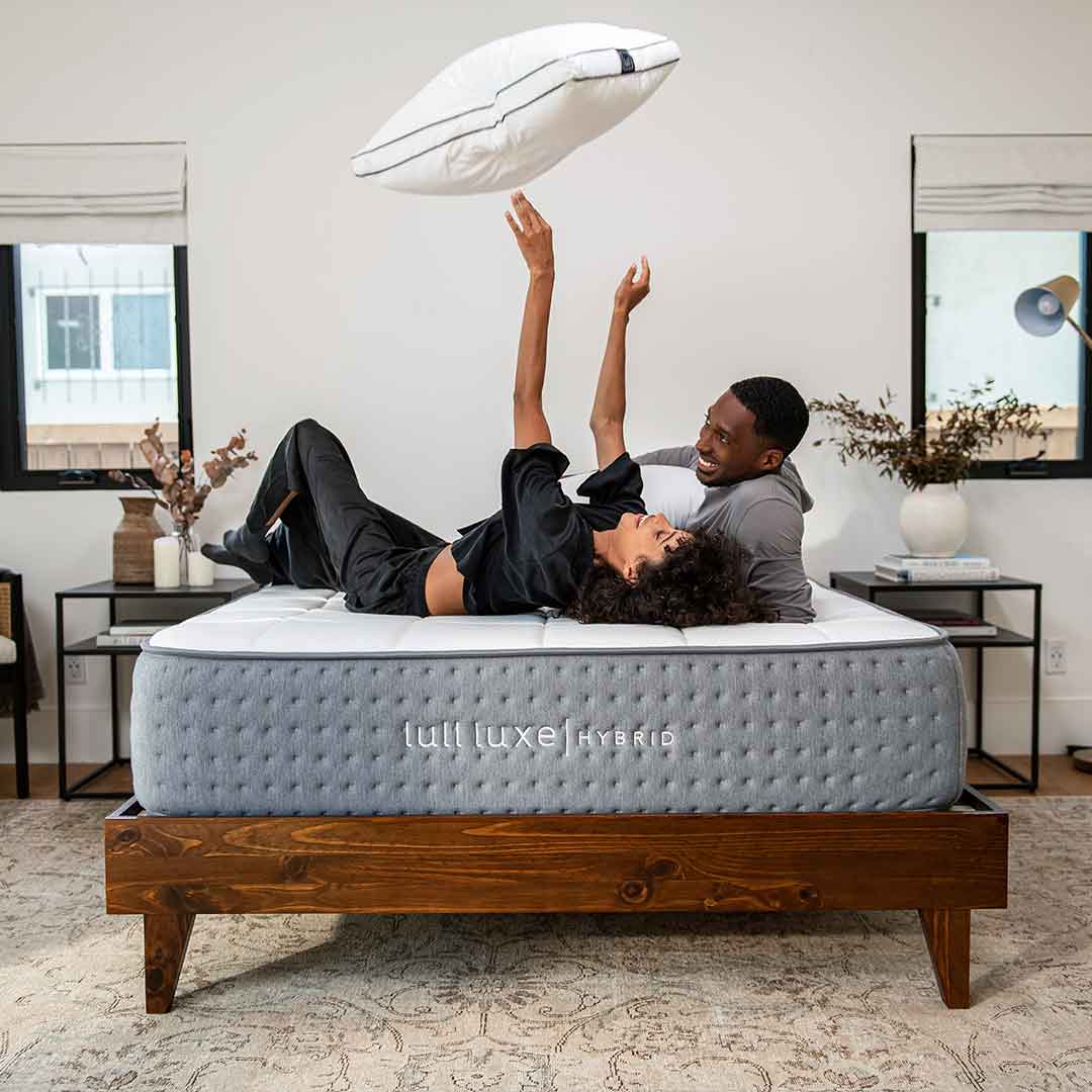 A happy couple on a mattress throwing a pillow in the air