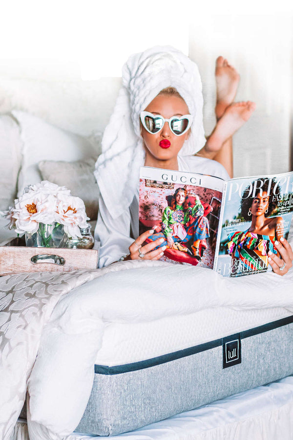 A woman in her robe laying on a lull mattress reading a fashion magazine.