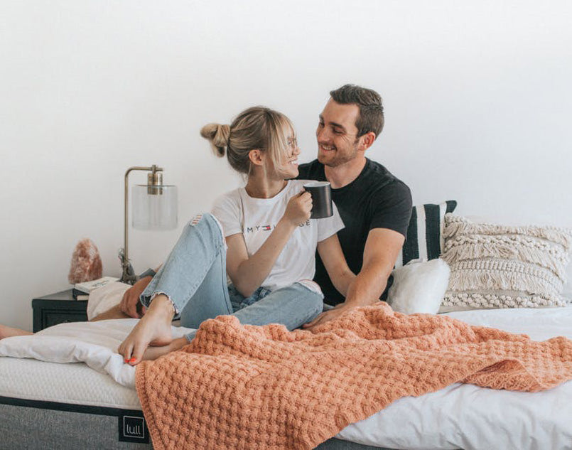 A happy couple sitting on a lull mattress with a cup of coffee.