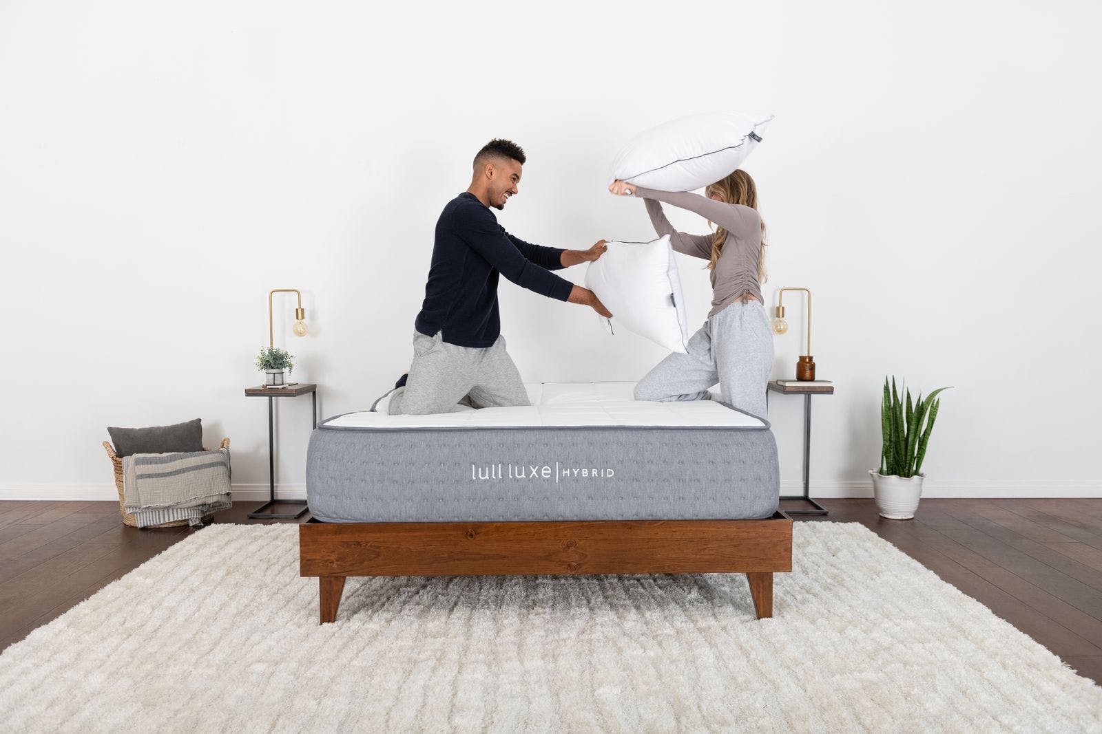 A couple smiling while having fun pillow fighting on top of a lull luxe mattress.
