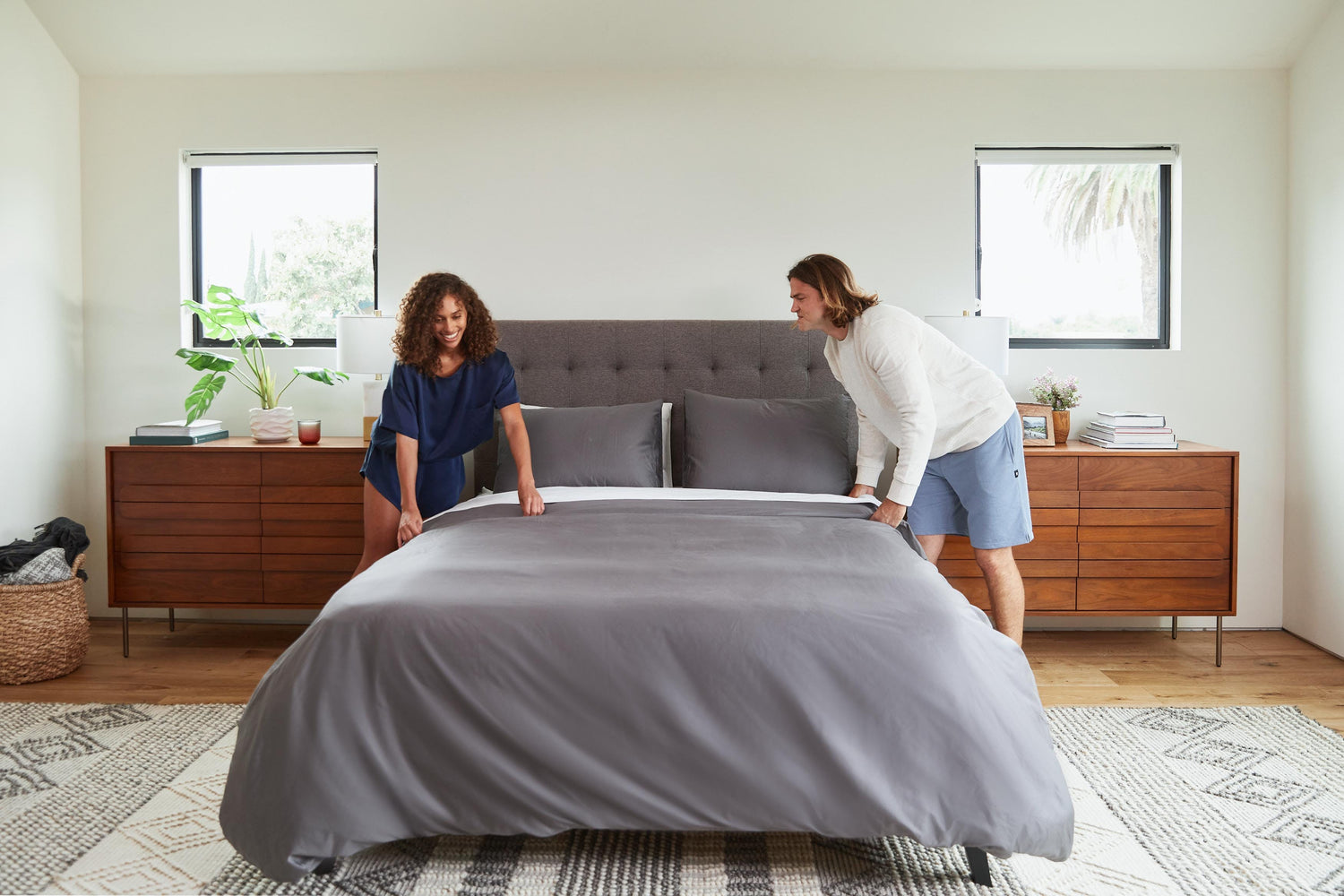 Couple making bed with granite grey sheets