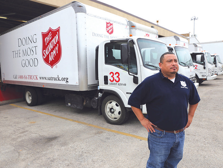 A salvation army truckyard with a proud employee in front. 