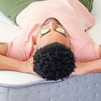 A man laying down with cucumbers on his eyes.